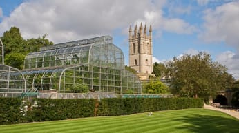 A large greenhouse, with the spire of Magdalen College in the background, and a manicured lawn in the foreground.
